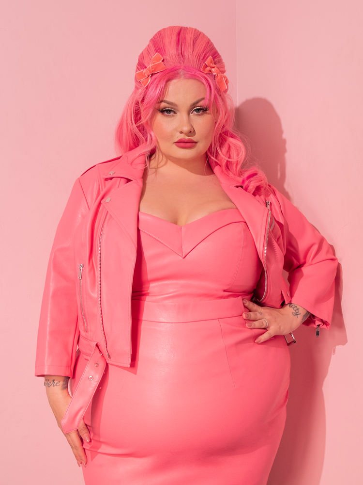 Embark on a journey to the glamorous past as the captivating model showcases the Bad Girl 3/4 Sleeve Cropped Motorcycle Jacket in Flamingo Pink Vegan Leather, a treasured creation from Vixen Clothing, the go-to destination for retro dress and vintage enthusiasts.