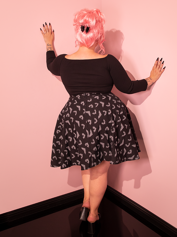 Immerse yourself in vintage chic as a pin-up style muse elegantly wears the Maneater Skater Skirt in its bewitching Glow-in-the-Dark Bat Print within the entirely pink showroom.