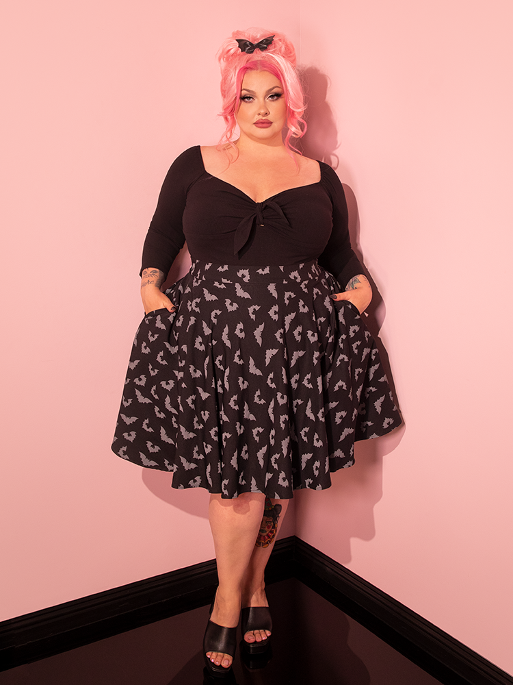 Exuding timeless allure, a pin-up model graces the pink-themed showroom, donned in the Maneater Skater Skirt featuring the mesmerizing Glow-in-the-Dark Bat Print.