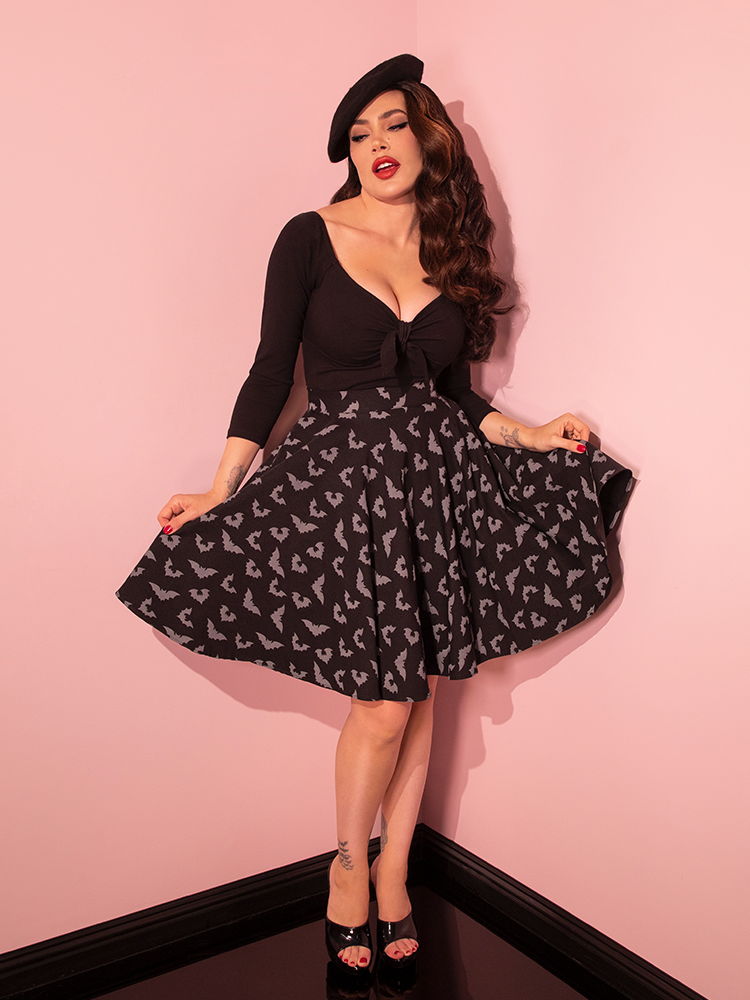 Step into a world of vintage allure as a pin-up style enchantress dons the Maneater Skater Skirt featuring the luminous Glow-in-the-Dark Bat Print, set against an all-pink backdrop.