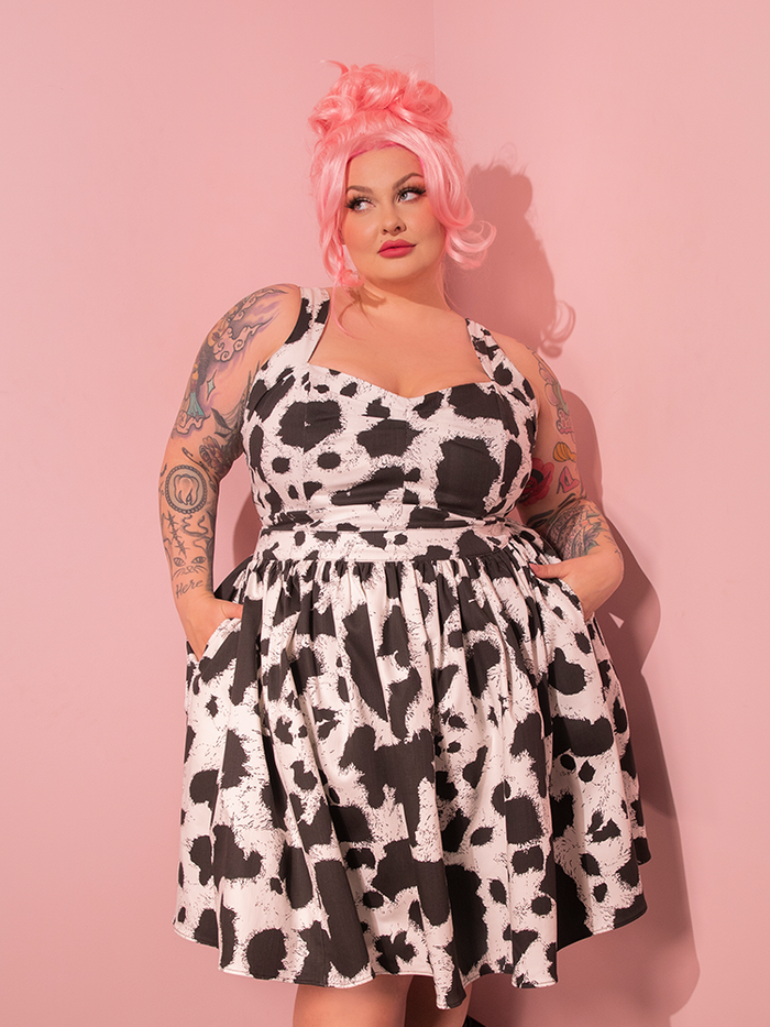 In a scene straight out of a retro fashion magazine, the lovely female model strikes a pose, showcasing the Vixen Skater Skirt in Cow Print, a true gem from the vintage-inspired brand, Vixen Clothing.