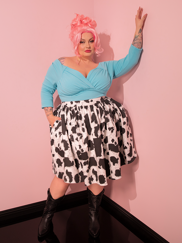 Channeling the essence of bygone eras, the female model effortlessly embodies the vintage flair of Vixen Clothing as she displays the Vixen Skater Skirt in Cow Print, a true treasure from the retro-inspired brand.
