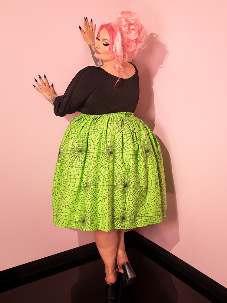 A female model effortlessly captures attention while wearing the Vixen Swing Skirt in Slime Green Spider Web Print, reflecting the nostalgic vibes of Vixen Clothing.