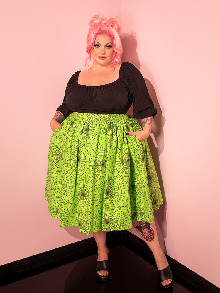 Embracing the essence of retro fashion, a female model presents the Vixen Swing Skirt in Slime Green Spider Web Print, a testament to Vixen Clothing's unique aesthetic.