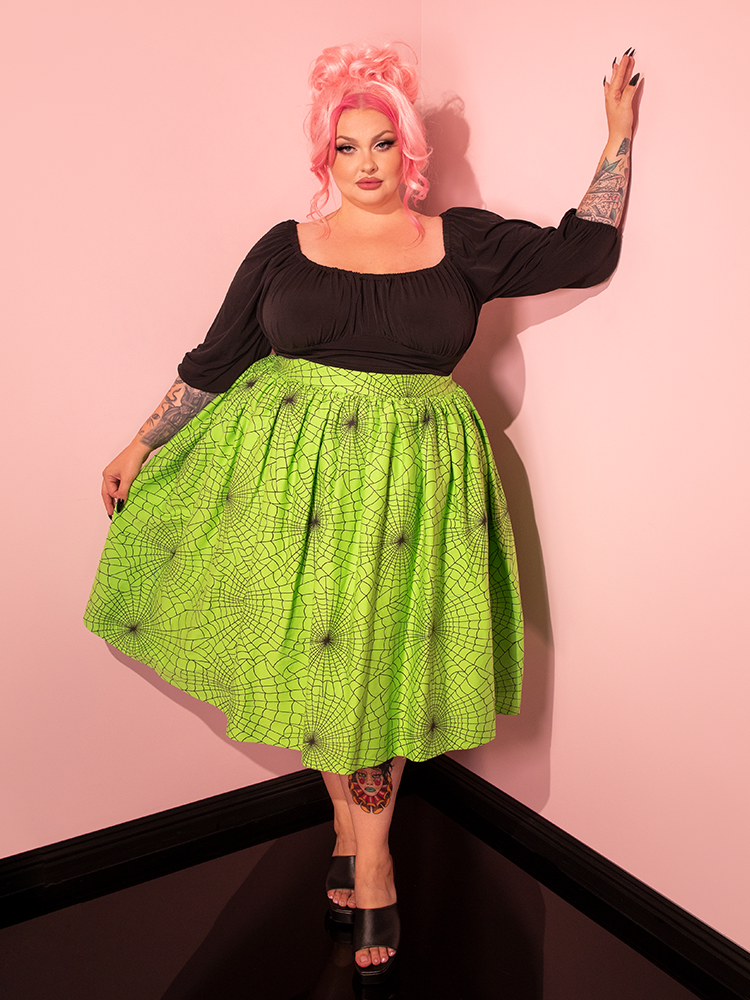 The Vixen Swing Skirt in Slime Green Spider Web Print graces the spotlight as a female model showcases it with poise, representing the distinctive style of Vixen Clothing.
