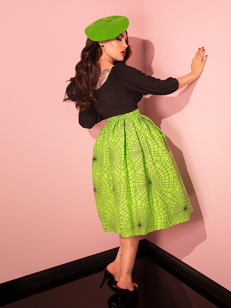 With a nod to nostalgia, a female model proudly exhibits the Vixen Swing Skirt in Slime Green Spider Web Print, illustrating the artistry of Vixen Clothing's retro fashion.