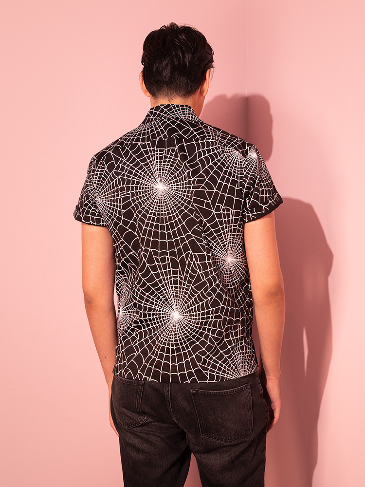 Showcasing the allure of Vixen Clothing's retro designs, a male model poses confidently in the Halloween Spider Web Print Button Up Short Sleeve Shirt in Black.