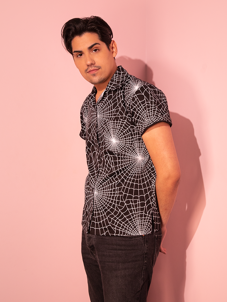 The Halloween Spider Web Print Button Up Short Sleeve Shirt in Black from Vixen Clothing takes center stage as worn by a male model in a captivating pose.
