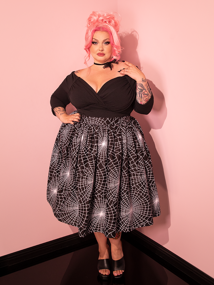 The glamorous embodiment of vintage allure, our lovely model graces the scene in the fresh Vixen Swing Skirt featuring the Black Spider Web Print, a masterpiece hailing from the illustrious Vixen Clothing.