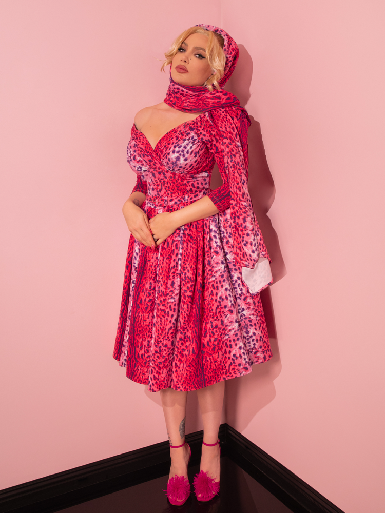 With a touch of vintage charm, a seductive model exudes elegance while showing off the Pink Leopard Print Starlet Swing Dress and Scarf by Vixen Clothing, a beloved retailer known for its retro fashion.