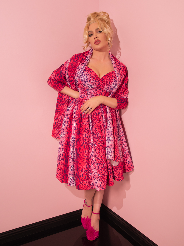 Embodying retro sophistication, a seductive model exudes confidence while wearing the Pink Leopard Print Starlet Swing Dress and Scarf by Vixen Clothing, a retailer synonymous with vintage fashion.