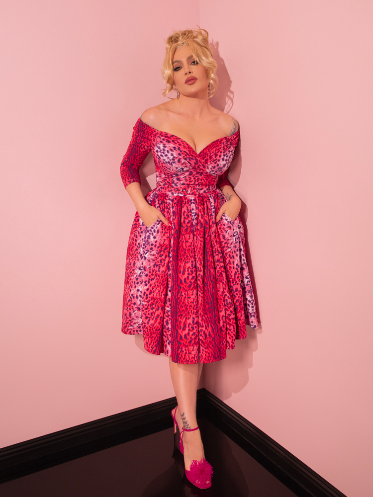 Embracing retro chic, a captivating model mesmerizes with her seductive demeanor while donning the Pink Leopard Print Starlet Swing Dress and Scarf from Vixen Clothing, a retailer specializing in vintage fashion.