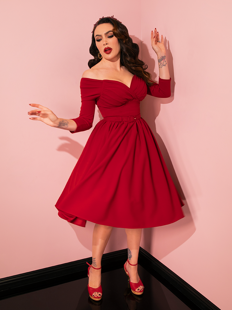 The stunning Micheline Pitt graces the scene in Vixen Clothing's Wrap Top in Red Velvet, portraying the brand's commitment to crafting elegant and timeless retro dress styles.