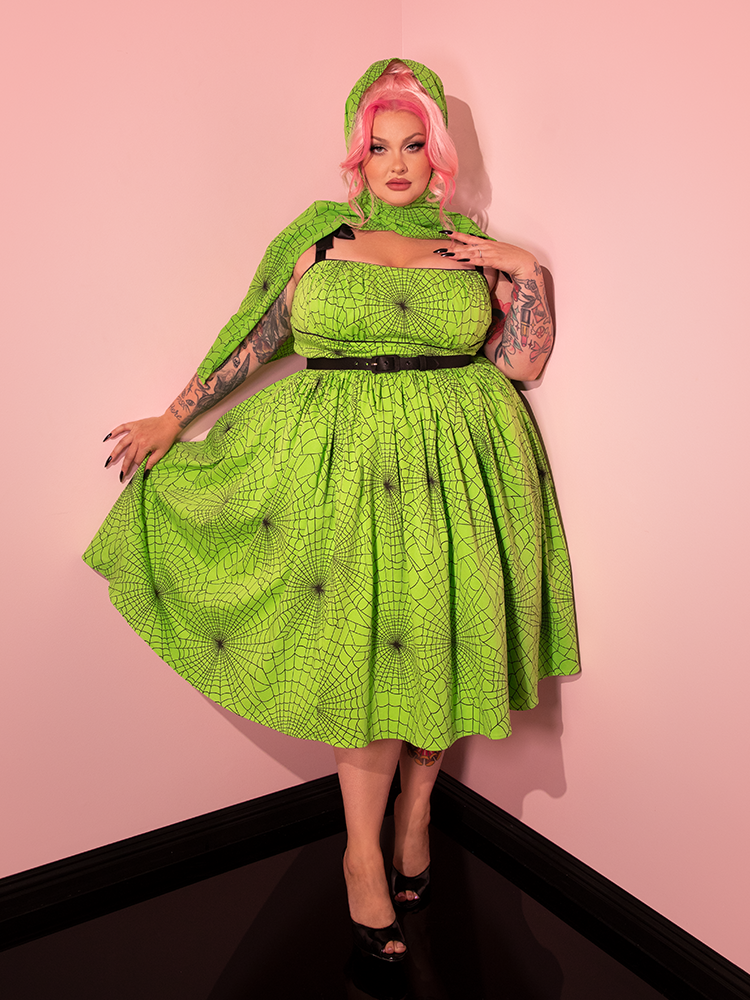 Embrace the allure of retro style as a stunning female model elegantly wears the 1950s Swing Sundress and Scarf, adorned in Playful Slime Green Spider Web Print from Vixen Clothing.