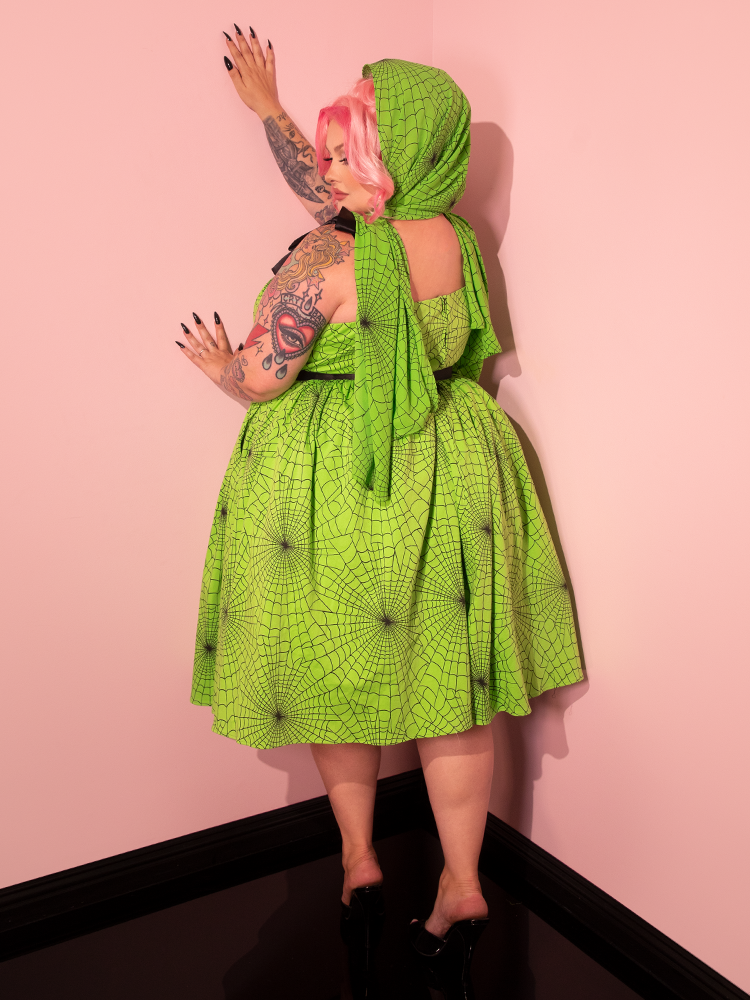 Step into the world of fashion with a gorgeous female model wearing the 1950s Swing Sundress and Scarf in Eye-catching Slime Green Spider Web Print, a stylish creation by Vixen Clothing's retro collection.