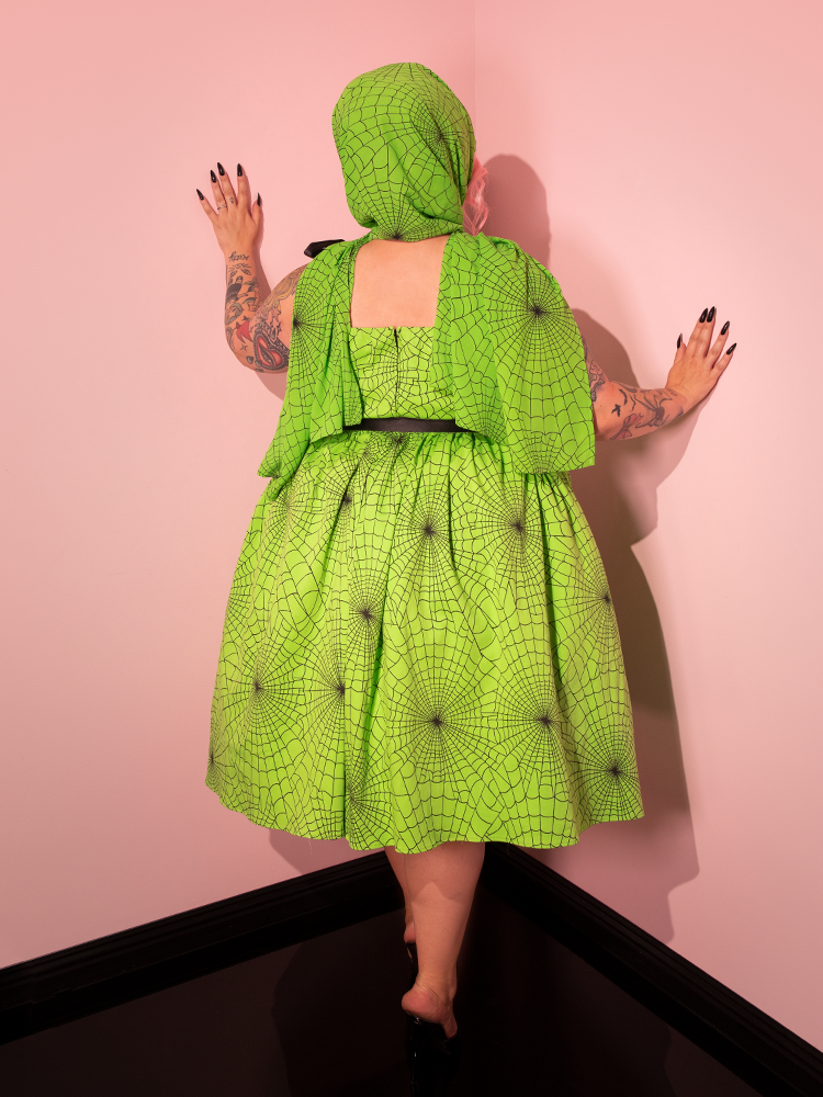 Let the beauty of a female model captivate you as she dons the 1950s Swing Sundress and Scarf, featuring Stunning Slime Green Spider Web Print, designed by the retro dress and clothing brand Vixen Clothing.