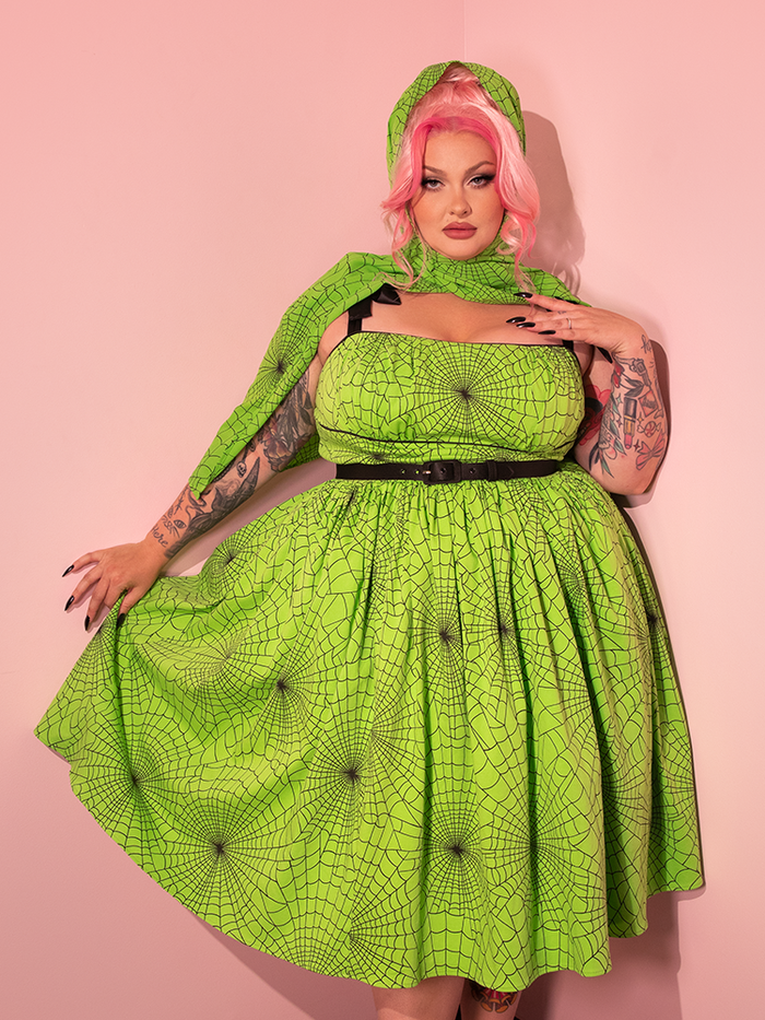 A stunning female model showcases the 1950s Swing Sundress and Scarf in Striking Slime Green Spider Web Print, courtesy of the retro dress and clothing brand Vixen Clothing.