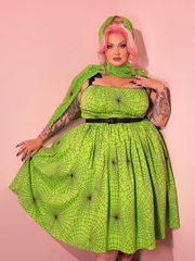 A stunning female model showcases the 1950s Swing Sundress and Scarf in Striking Slime Green Spider Web Print, courtesy of the retro dress and clothing brand Vixen Clothing.
