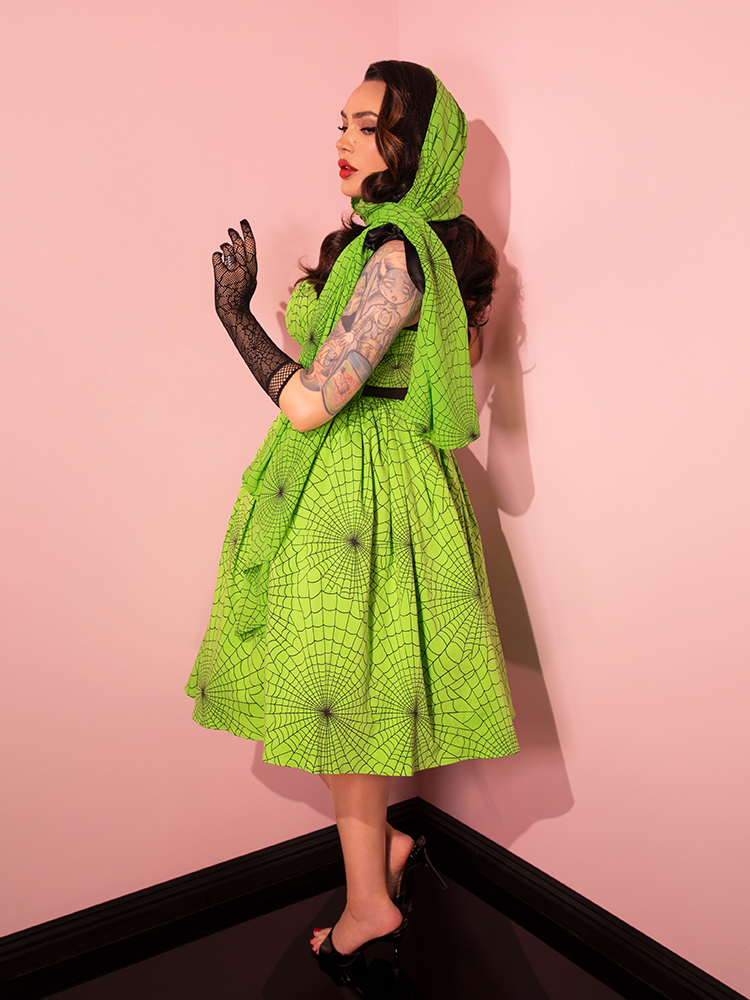 Discover Vixen Clothing's latest addition with a stunning female model wearing the 1950s Swing Sundress and Scarf in Vibrant Slime Green Spider Web Print, a tribute to retro fashion.