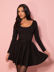 A vintage-inspired black swing mini dress displayed against a pink wall, highlighting its flared skirt and elegant neckline that echo classic Hollywood glamour.