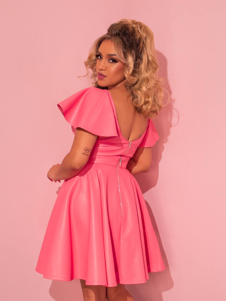 Nostalgia takes center stage as the stunning model presents the Flamingo Pink Vegan Leather Bad Girl Skater Skirt, a breathtaking vintage creation hailing from the prestigious retro dress maker Vixen Clothing.