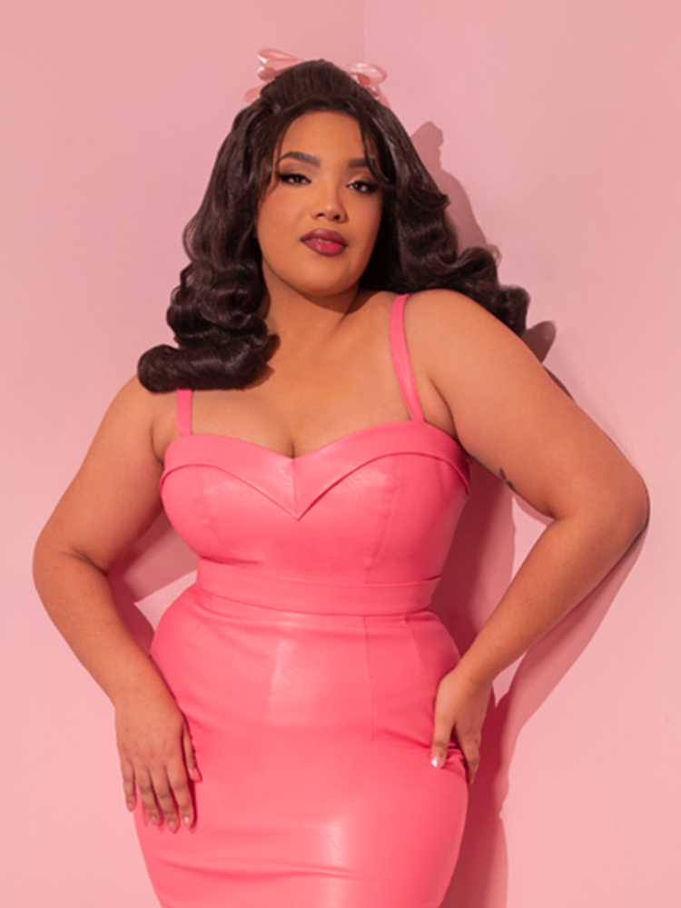 Take a step back in time and let the captivating model transport you to the golden era with the Bad Girl Maneater Top in Flamingo Pink Vegan Leather, an enchanting creation by Vixen Clothing, the ultimate destination for retro enthusiasts.