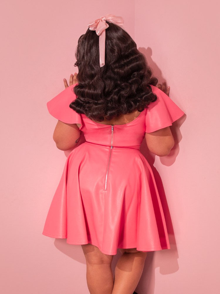 Embodied with retro flair, the stunning model effortlessly showcases the Flamingo Pink Vegan Leather Bad Girl Skater Skirt, a captivating piece of vintage fashion crafted by the talented designers at Vixen Clothing.