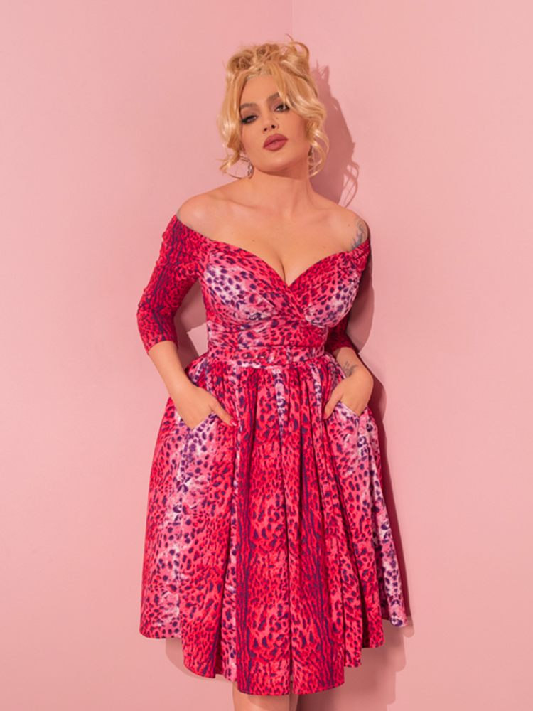 Embracing the vintage aesthetic, a captivating model strikes a seductive pose while donning the Pink Leopard Print Starlet Swing Dress and Scarf from Vixen Clothing, a retailer renowned for its retro-inspired collection.