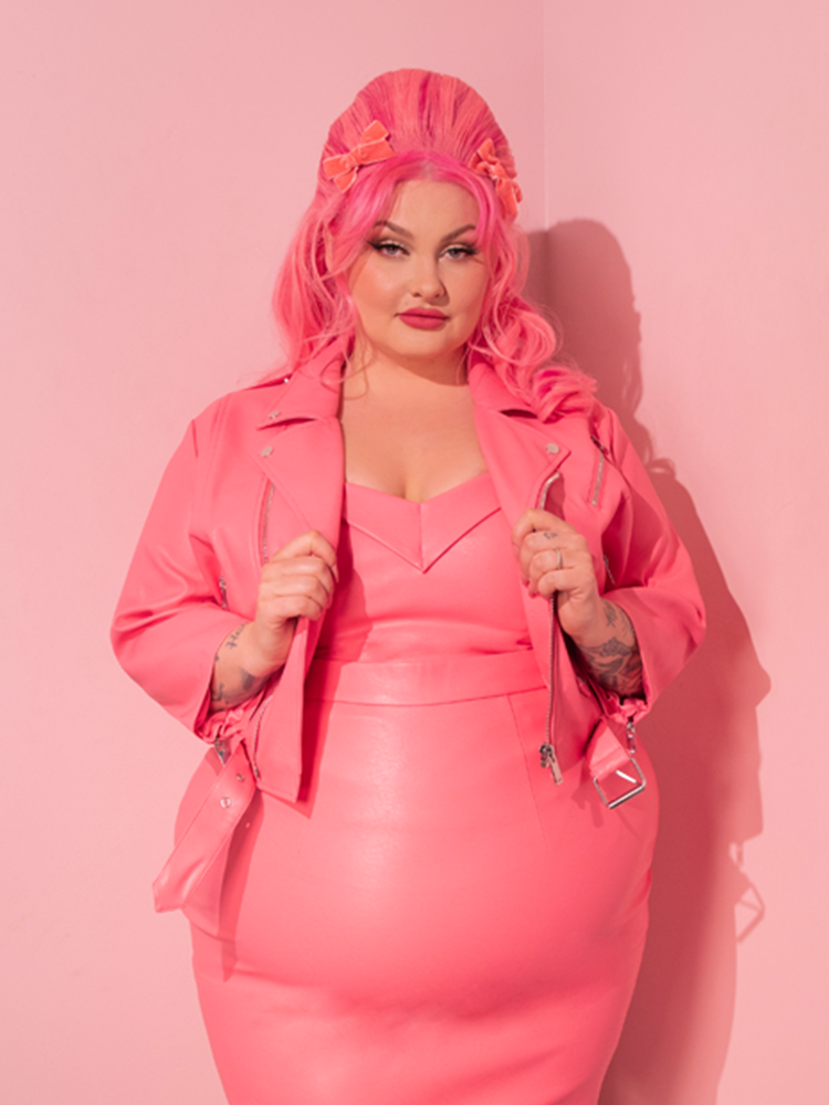 Delight in the sight of the ravishing model, embodying the essence of retro fashion with the Bad Girl 3/4 Sleeve Cropped Motorcycle Jacket in Flamingo Pink Vegan Leather, a prized possession from the renowned vintage clothing brand, Vixen Clothing.