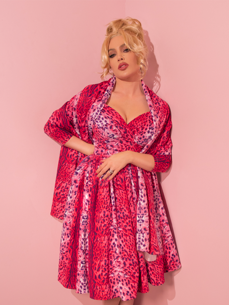 Evoking the charm of bygone eras, a seductive model exudes allure while modeling the Pink Leopard Print Starlet Swing Dress and Scarf, a stunning creation by Vixen Clothing, a beloved retro dress and clothing retailer.
