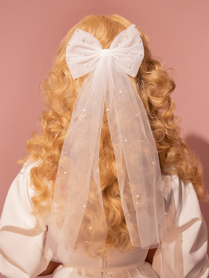 This large ivory mesh bridal hair bow, adorned with delicate pearl accents, exudes a vintage charm perfect for achieving that classic Hollywood bridal look.