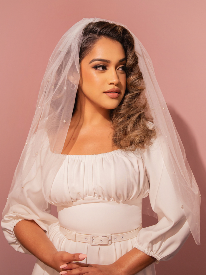 This delicate tulle veil, embellished with pearl bead accents on white mesh, channels a vintage-inspired bridal elegance perfect for your classic Hollywood moment.
