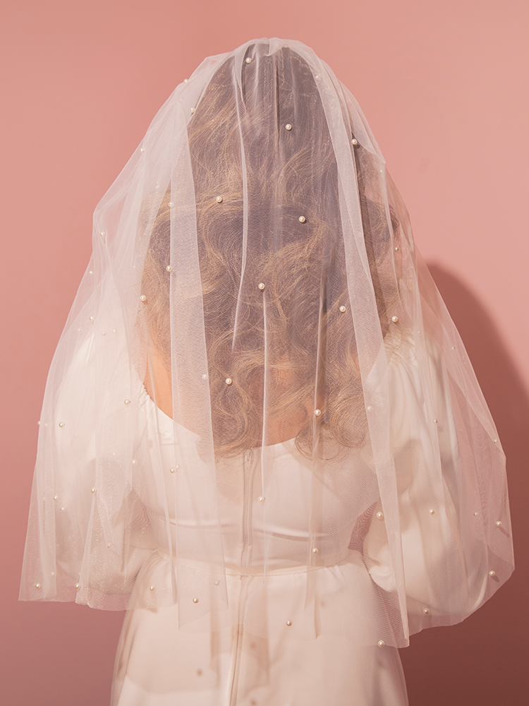 Embrace the charm of yesteryear with this white mesh tulle veil, beautifully accented with pearls, creating a vintage aesthetic for your special day.