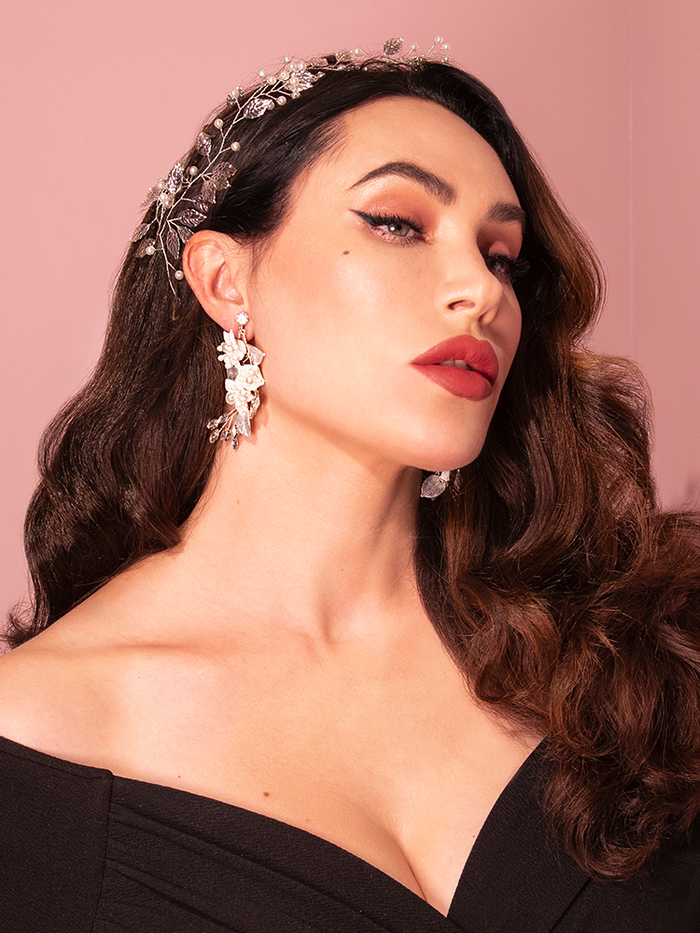 A playful brunette model exudes charm while posing in the Vintage-Style Leaf and Pearl Hair Wire in Silver from the retro clothing brand Vixen Clothing.