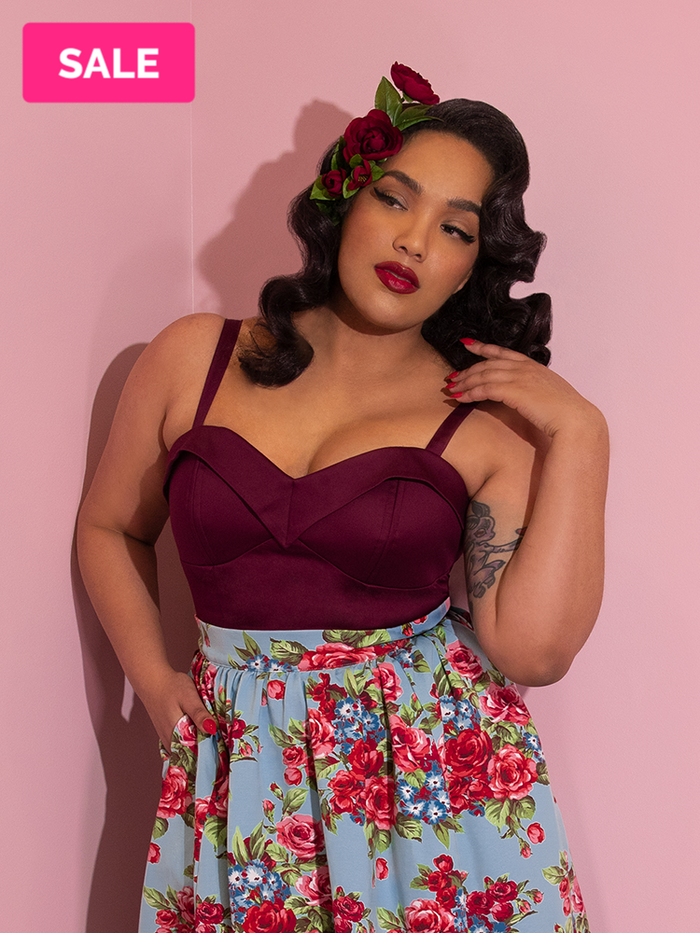A closeup of Ashleeta modeling the Vixen Clothing Maneater top in dark berry paired with hair flowers and a blue floral skirt.