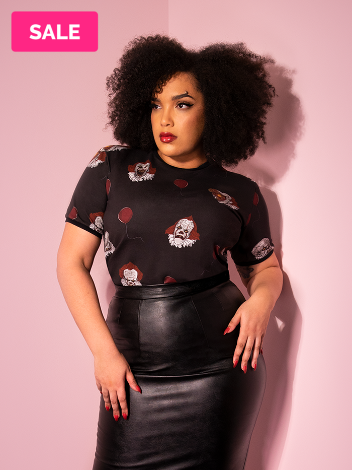 Looking just off camera with her hands on her hips, Ashleeta models the Pennywise ringer tee by Vixen Clothing.