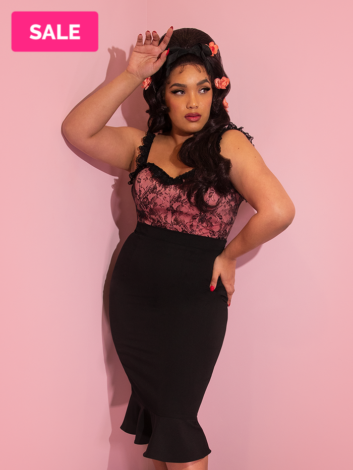 A closeup of Ashleeta with pink flowers in her hair modeling the Vixen flutter skirt in black paired with a peach and black lace bustier top.