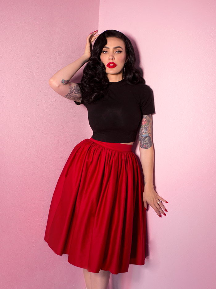 Looking straight out of classic Hollywood, Micheline Pitt looks directly into the camera while wearing the Swing Skirt in Red and a short sleeve black top.