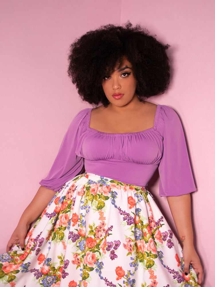 A closeup of Ashleeta looking at the camera modeling the Vacation top in lavender paired with a white floral skirt.