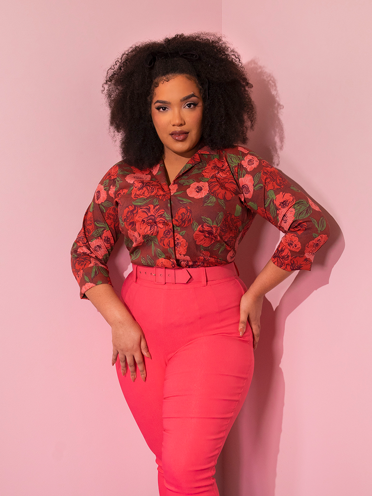 Shot from the knees up, African American model wears the 1950's Vintage Style Button Up Blouse in Chocolate Roses tucked into pink cigarette pants. 