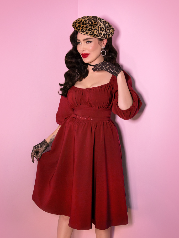 Micheline Pitt smiles while looking off camera while wearing the Ruby Red Vacation Dress with leopard beret.