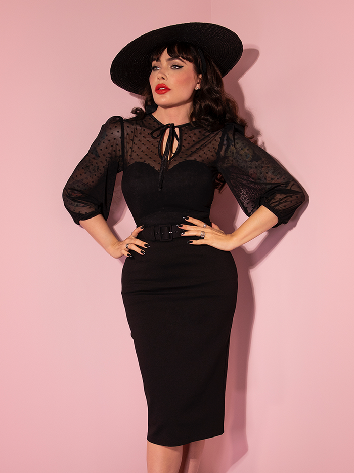 Micheline Pitt posing with her hands on her hips and looking off-camera while wearing the Frenchie Wiggle Dress in Black