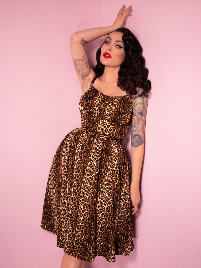Seductively posed against a pink background, Micheline Pitt models the Ingenue Dress in Leopard Print.