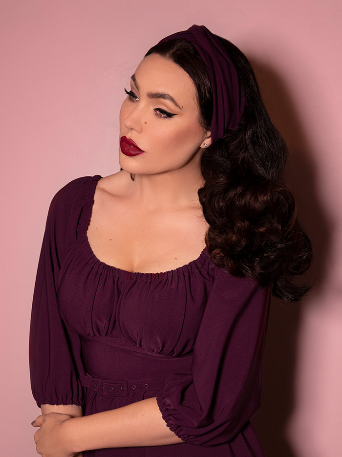 A closeup shot of Micheline Pitt modeling the vintage style knot headband in eggplant paired with a matching dress.