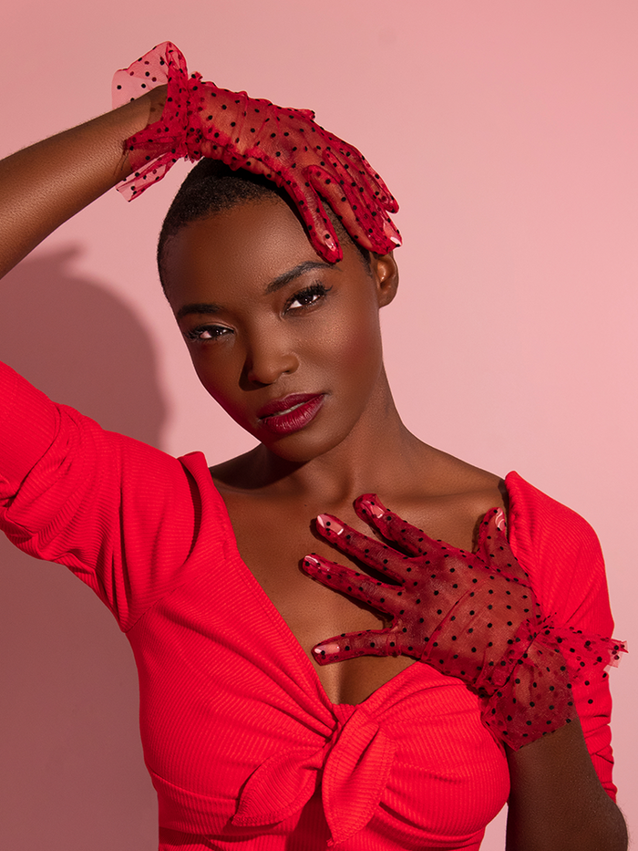 Brittany poses with her hands in different positions to accentuate the Mesh Polka Dot Gloves in Red from retro clothing company Vixen Clothing.
