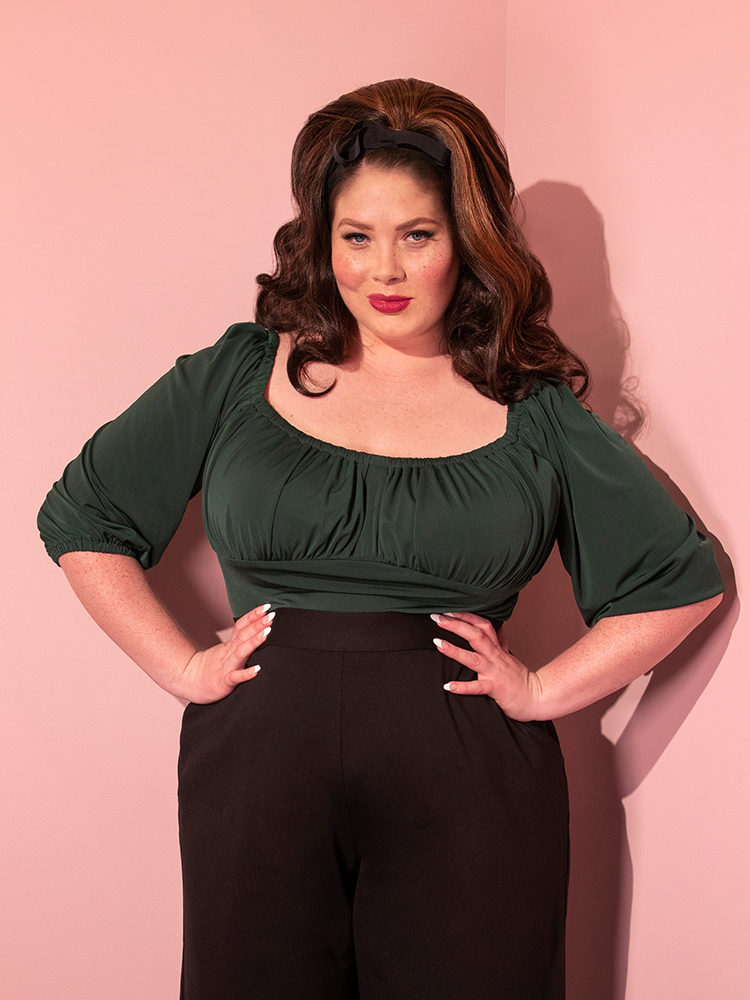 Model wearing the Vacation Blouse in Hunter Green tucked into black pants from Vixen Clothing.
