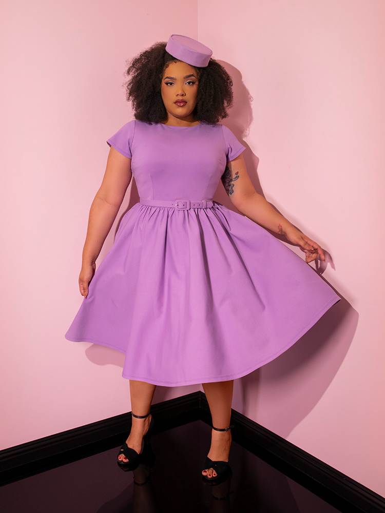 Model standing and looking directly into the camera while the skirt on the Avon Swing Dress in Lilac flows around..