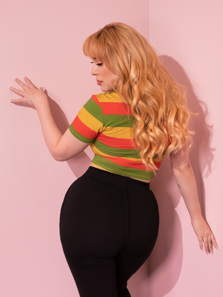 Model facing away from the camera wearing the Bad Girl Crop Top in Orange/Yellow/Avocado Stripes with black retro cigarette pants.