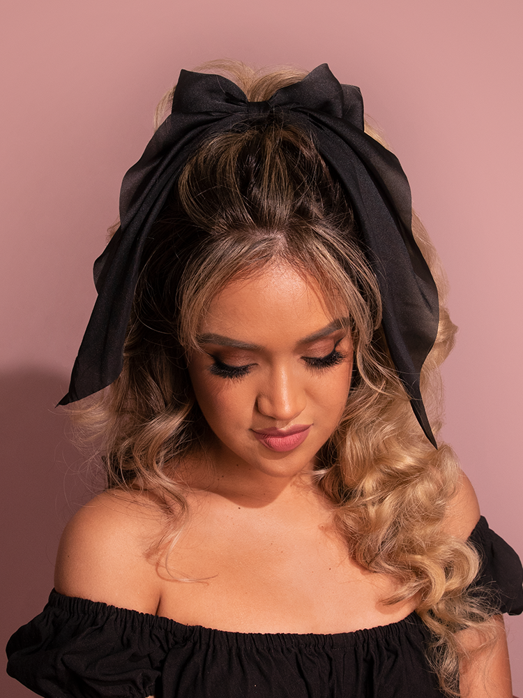 Modeling the retro-inspired Large Satin Hair Bow in Black, the female model epitomizes retro elegance from Vixen Clothing's collection.