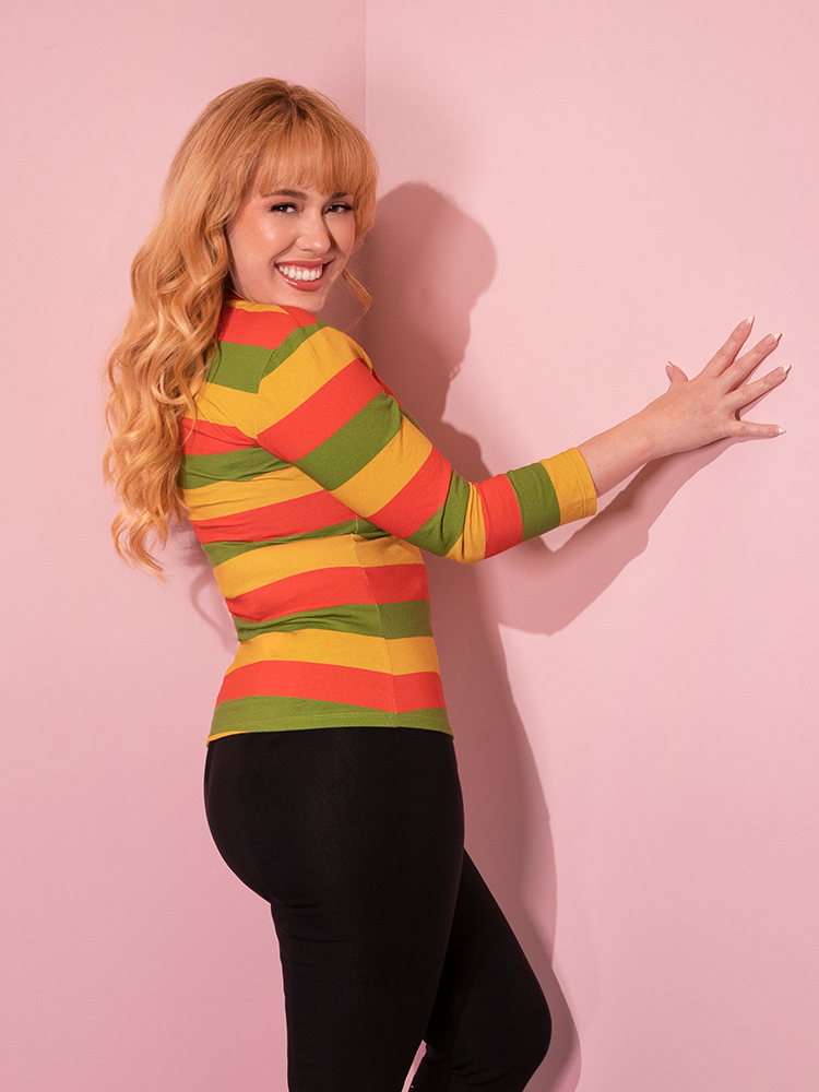 Model turned to the side shows off the colors of the Bad Girl 3/4 Sleeve Top in Orange/Yellow/Avocado Stripes being worn over black stretchy pants.
